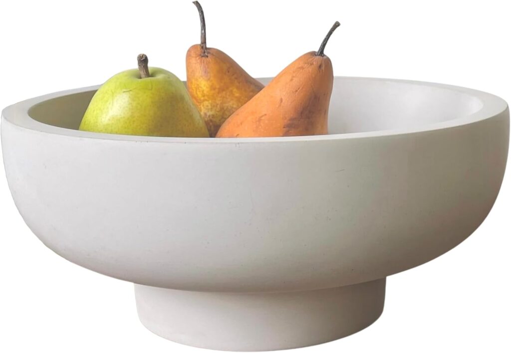 A modern, round fruit bowl made of light-colored material, containing a green apple and two brown pears.